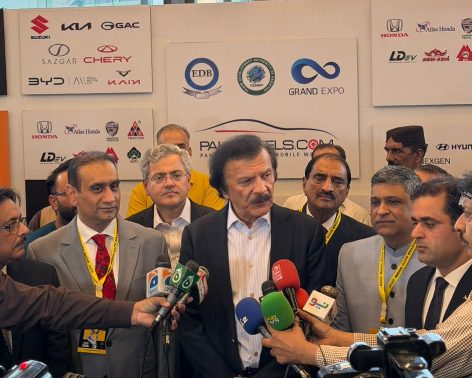 Industry leader answering questions from a press scrum in front of exhibitor logos